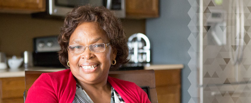 An African-American woman with glasses smiles in her kitchen.